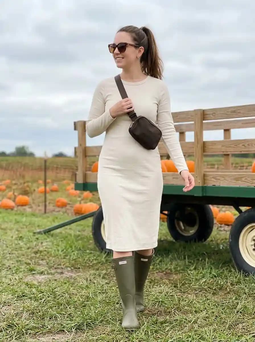 Cream long-sleeve midi dress with tall olive rain boots and dark crossbody belt bag
