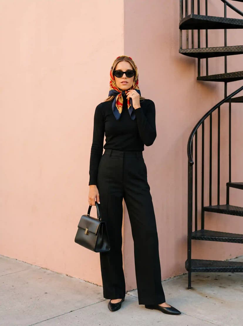 All-black ensemble with a fitted long-sleeve top, wide-leg trousers, silk print headscarf, and black cat-eye sunglasses