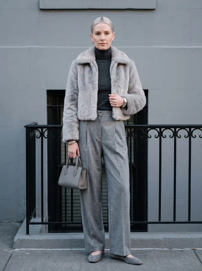 Dark charcoal grey fitted turtleneck, medium grey pleated wide-leg wool trousers, pale silver-grey faux fur cropped jacket, and grey suede pointed-toe flats