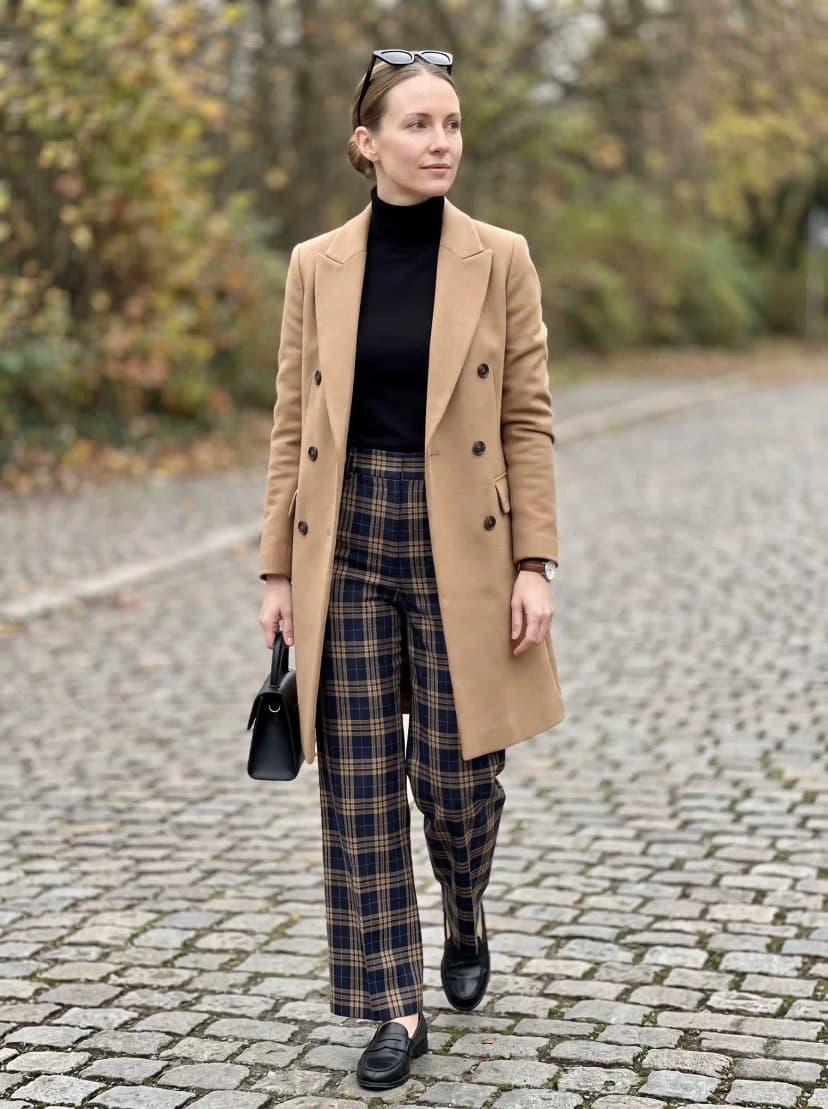 Black turtleneck, plaid wide-leg trousers, camel wool coat, black penny loafers, and black handbag