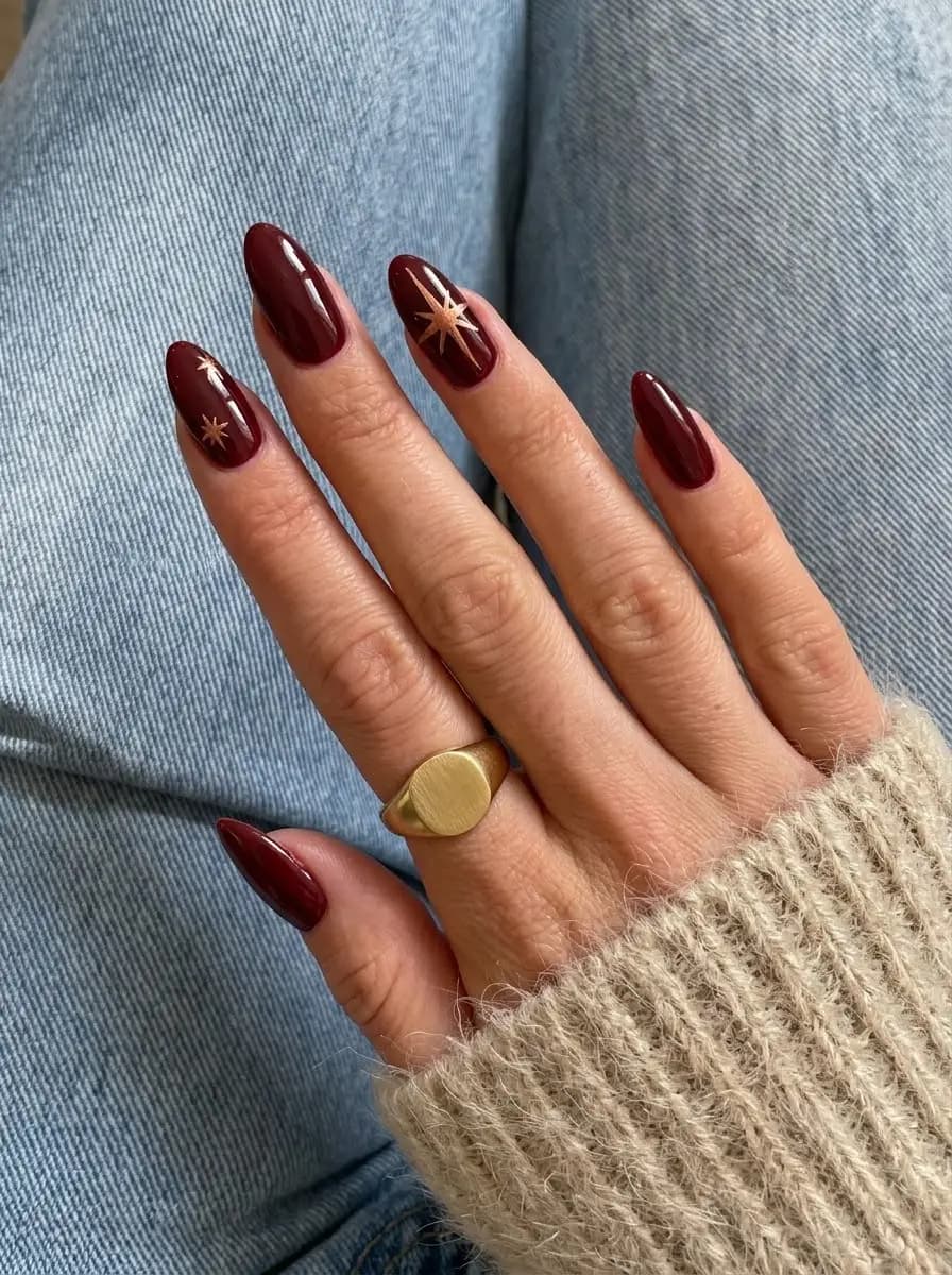 Deep burgundy Christmas nails with delicate metallic gold starburst accents