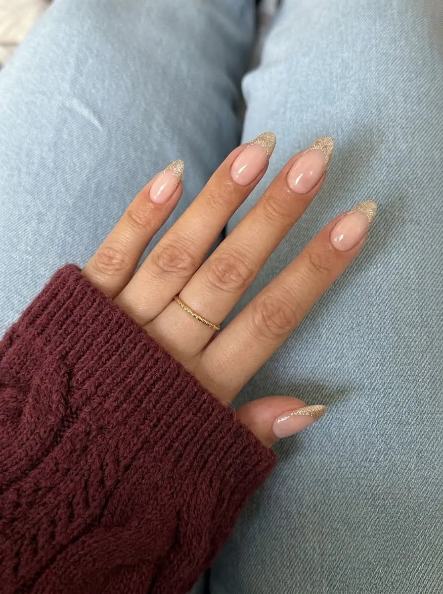 Nude French nails with champagne gold glitter tips on long almond nails