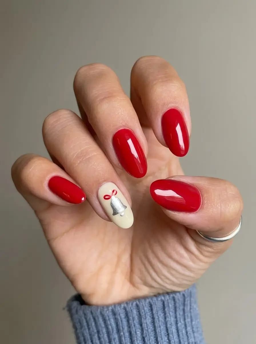 Glossy red Christmas nails with a miniature silver holiday bell and red bow accent