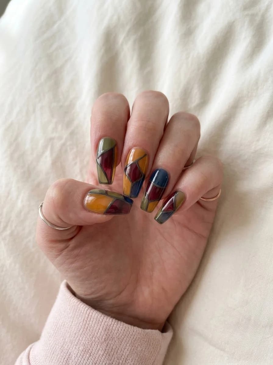 Artistic nails featuring mustard yellow, wine red, olive green, and navy sections divided by dark outlines like stained glass