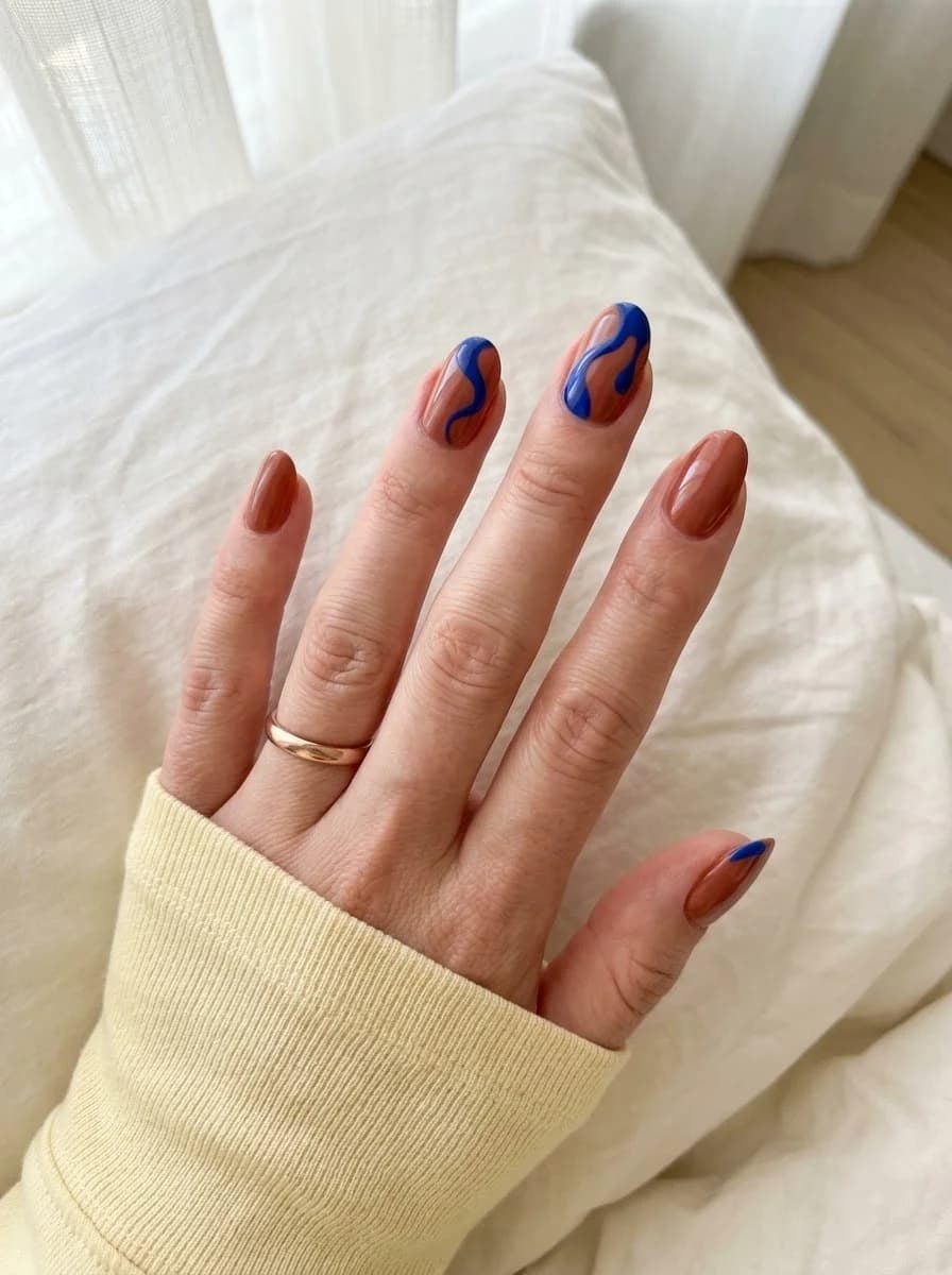 Short warm cinnamon brown nails with bold cobalt blue swirl linework on accent nails