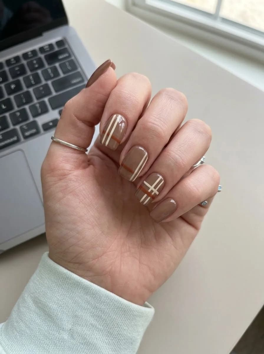 Short square nails with mocha brown base, cream and rust plaid lines, and cozy October styling