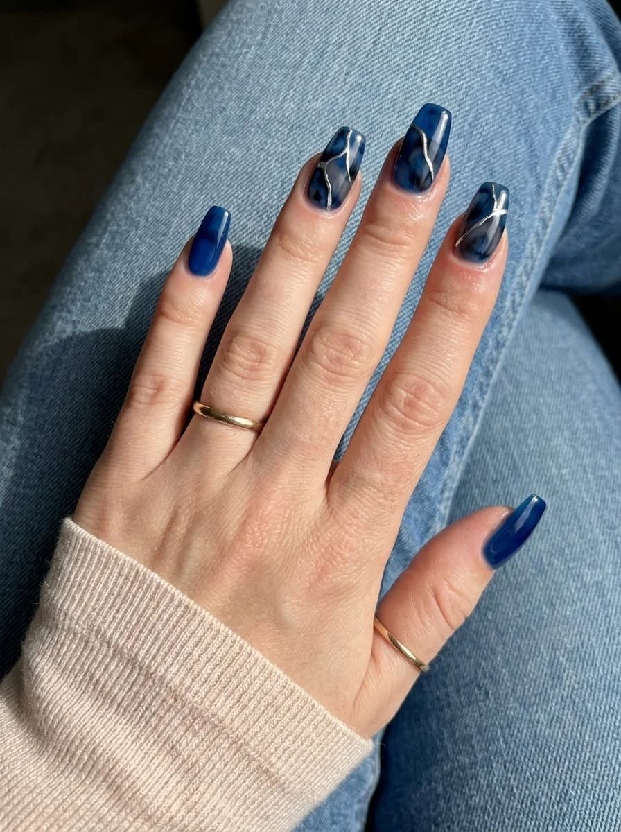 Deep cobalt and midnight blue marbled nails with thin metallic silver line details