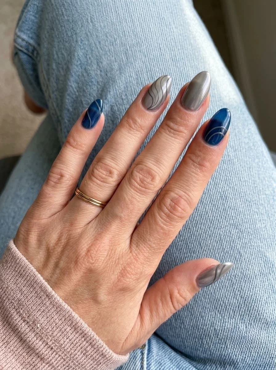 Almond nails with deep sapphire blue base and curved metallic silver wave linework