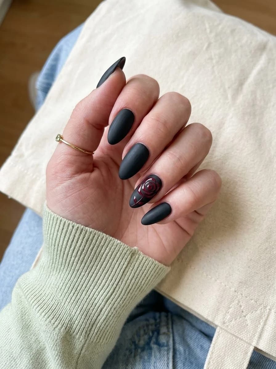 Matte black almond nails with a single dark burgundy-red rose accent nail